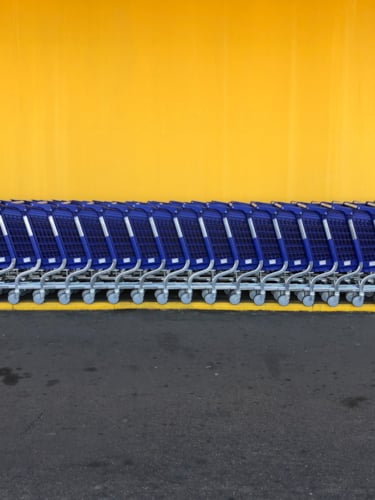 Empty blue shopping trolleys lined up against yellow wall