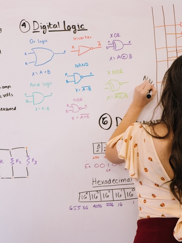 Young person seen from behind writing on a whiteboard Junior Academy