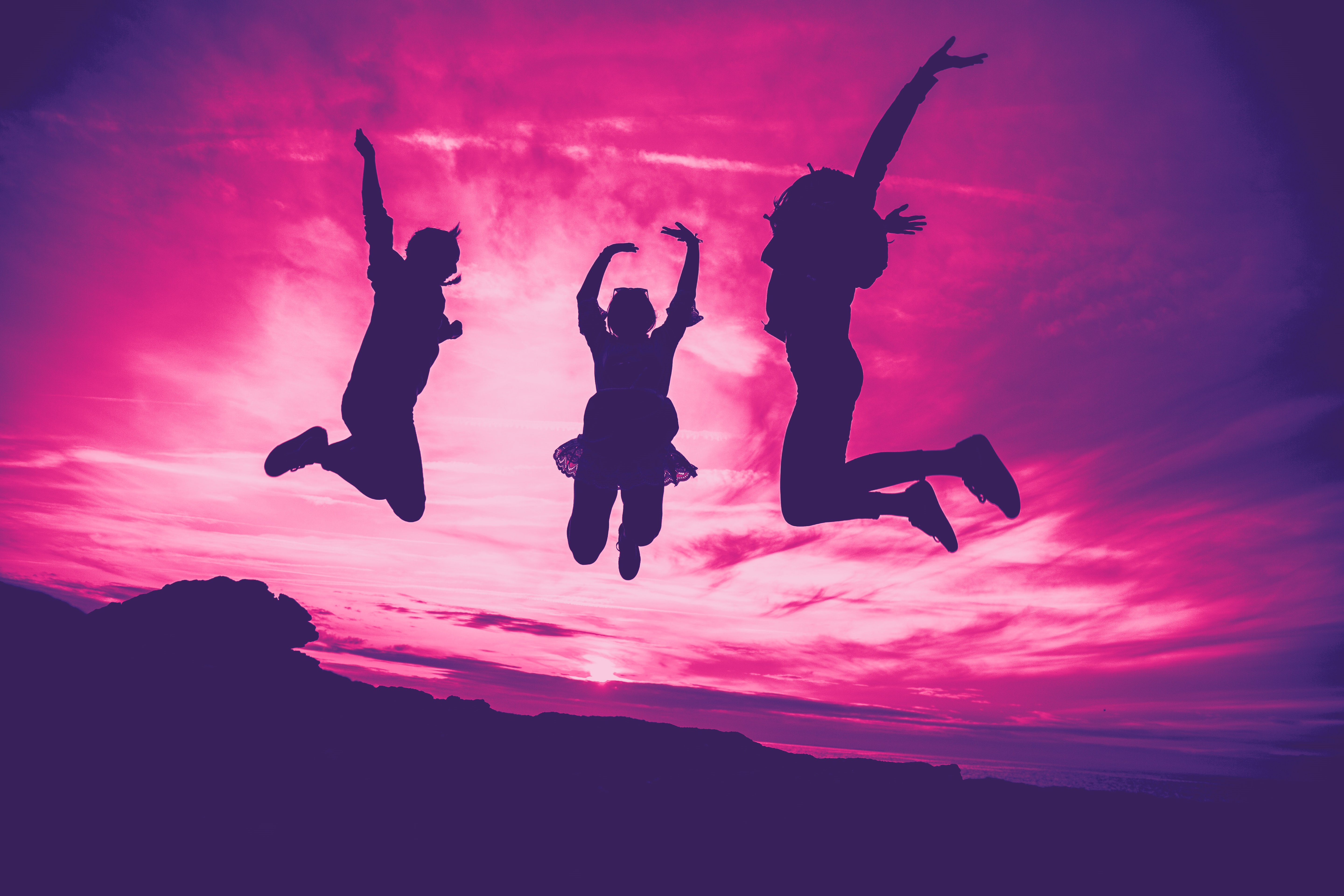 Tre personer som hoppar mot rosa himmel